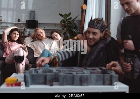 KIEW, UKRAINE - 27. JANUAR 2020: Selektiver Fokus von Männern in Feenkostümen Labyrinthspiel spielen, während gelangweilte Mädchen auf dem Sofa sitzen Stockfoto