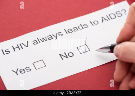 Zugeschnittene Ansicht der Person, die den HIV-Fragebogen auf rotem Hintergrund beantwortet Stockfoto
