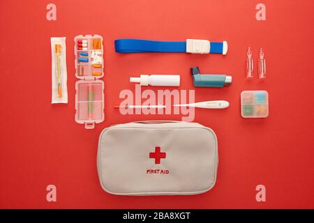 Flat Lay mit Erste-Hilfe-Kit, Pillen und medizinischen Gegenständen auf rotem Hintergrund Stockfoto