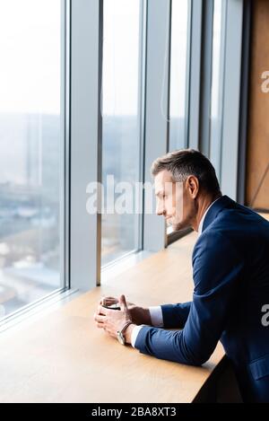 Seitenansicht des Geschäftsmannes in Anzug mit Glas und Blick durch Fenster Stockfoto