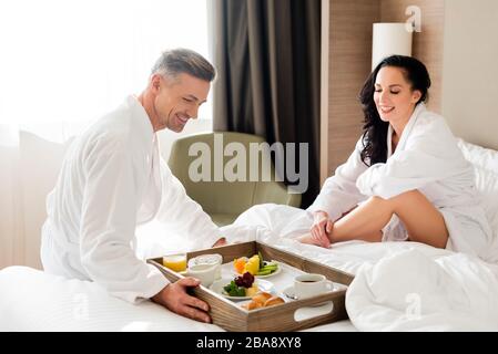 Freund, der Frühstück im Bett für lächelnde Freundin im Hotel mitbrachte Stockfoto