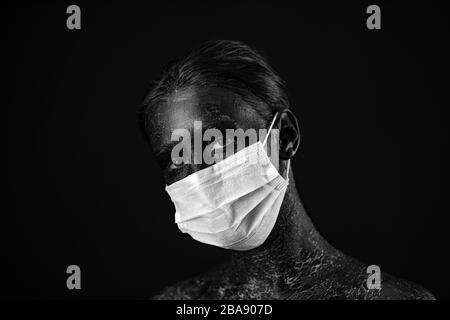 Coronavirus, maskierte Frau. Studio-Porträt einer jungen Frau, die eine Gesichtsmaske trägt, mit Blick auf die Kamera, auf schwarzem Hintergrund. Grippeepidemie, Staub Stockfoto