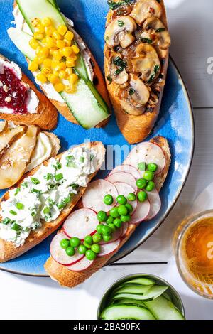 Verschiedene Bruschetta- oder Tapas-Sets mit verschiedenen herzhaften und süßen Belägen auf Platte und weißem Hintergrund. Toast-Sandwich mit Gemüse und Obst öffnen Stockfoto