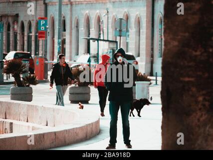 Mann, der eine Gesichtsmaske trägt und während des Ausbruchs des Corona-Virus telefoniert. Zwei Freunde, die hinten spazieren gehen, im Gegensatz zum ernsten und entspannten Peo Stockfoto