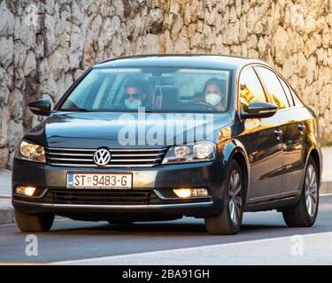 Ein Paar fährt einen schwarzen volkswagen, der beim Ausbruch des Corona-Virus Gesichtsmasken trägt. Pendeln zur Arbeit Stockfoto