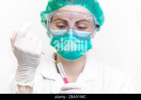 Weiblicher Arzt im Labor mit einem Blutschlauch zur Analyse und Probenahme von Coronavirus unter dem Mikroskop. Stockfoto