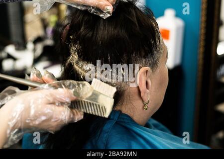 Attraktive Brünette gründlich färben Haare der weiblichen Klienten, während sie im Stuhl sitzt im Beauty Salon Friseur Stockfoto