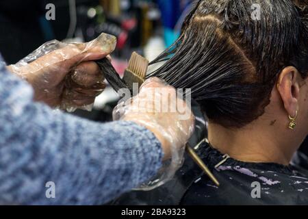 Attraktive Brünette gründlich färben Haare der weiblichen Klienten, während sie im Stuhl sitzt im Beauty Salon Friseur Stockfoto