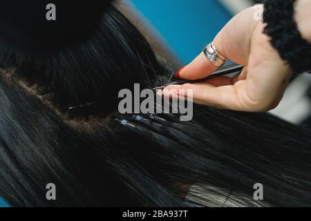 Professionelle Frau, die Haarverlängerungen mit verschiedenen Griffarten anwendet. Nano-Ringe-Verlängerungen aus echten Humas-Haaren. Stockfoto