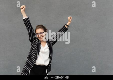 Eine junge gutaussehende Frau steht in einem Business-Anzug auf dem Hintergrund eines Bürogebäudes. Das Konzept einer erfolgreichen, selbstbewussten Geschäftsfrau. Stockfoto