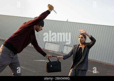 Ein Mann griff auf einem Parkplatz eine wehrlose Frau an, er versucht, ihr die Geldbörse zu nehmen. Stockfoto