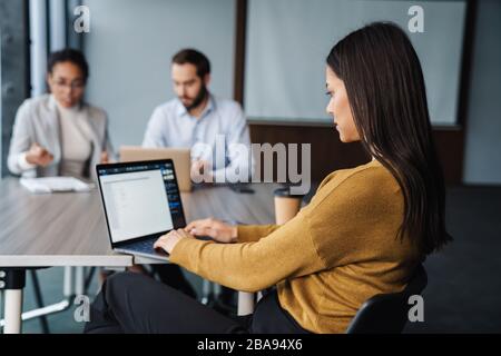Bild von multiethnischen jungen weiblichen und männlichen Kollegen, die am Tisch sitzen und an Laptops im Büro arbeiten Stockfoto