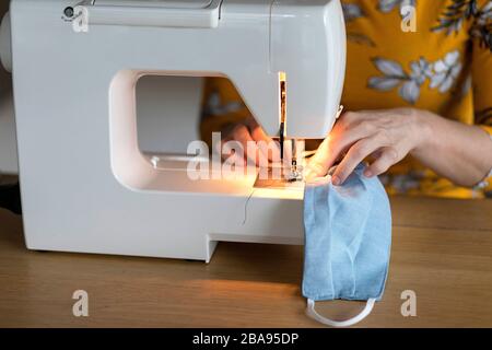 Frau, die in ihrer Wohnung hausgemachte Gesichtsmaske mit einer Nähmaschine anstellt, während sie unter Quarantäne steht, Schutz vor Corona-Viren, März 2020 Stockfoto