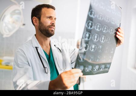 Porträt des jungen gutaussehenden Arztes, der Röntgenstrahlung im Krankenhaus überprüft Stockfoto