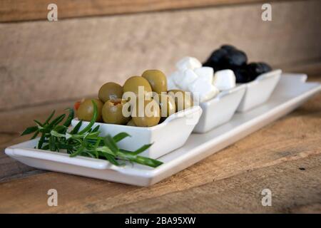 Nahaufnahme der Platte mit Oliven, Fetakäse und Rosmarin auf Holzbrett Stockfoto