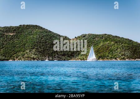 Griechenland ithaki-insel, weiße Segelyacht im offenen blauen Meer mit grüner Insel im Hintergrund. Stockfoto