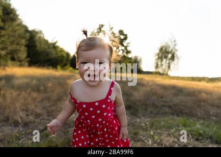 Kleines Mädchen spielt in der Natur. Baby Mädchen haben Spaß im Park und laufen barfuß auf dem grünen Gras. Lustige und unbeschwerte Kindheit. Stockfoto