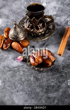 Orientalische Datteln in einer Untertasse im ethnischen Stil mit einem Glas Tee und Zimtstäbchen Stockfoto