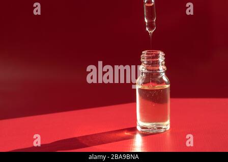 Kosmetik in einer transparenten Flasche mit einem Tropfer auf rotem Hintergrund. Harte Schatten. Platz für Text Stockfoto