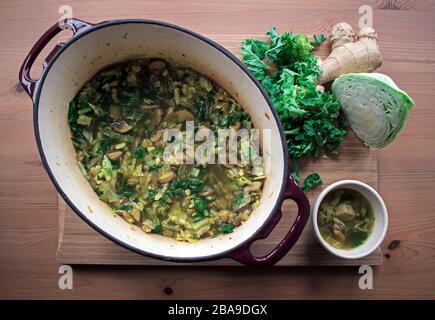 Gesundheitsspeisen - immune Suppe aus Kale, Kohl, Ingwer und Pilzen, die über den Kopf geschossen wurden, auf einem Holzbrett schön angeordnet. Stockfoto