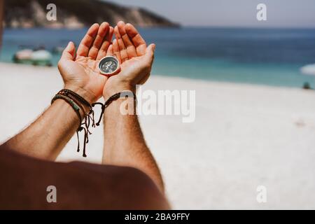 n's Hand, der den Kompass hält. Strand und Meer im Hintergrund Reisekonzept, Sommerurlaub, Urlaub und Reise. Stockfoto