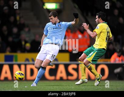 Der Manchester-City-Torhüter Edin Dzeko (links) hat einen Schuss auf Tor, der Norwich-City-Torhüter Mark Bunn (nicht im Bild) für ein Eigentor und den vierten seiner Mannschaft abgibt. Stockfoto