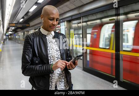 Eine Frau benutzt ihr Smartphone auf einer U-Bahn-Plattform der Jubilee Line, die Teil des U-Bahn-Systems London Underground ist Stockfoto