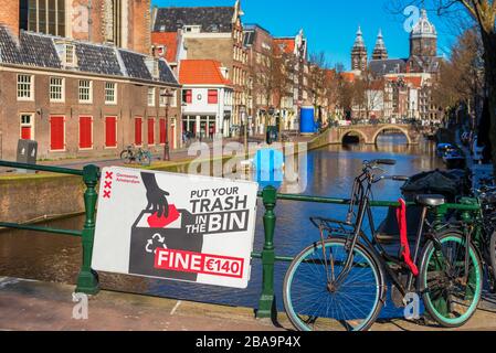 Warnschild auf Englisch über einem Kanal mit der Aufschrift "Put Your Trash in the bin" im Rotlichtviertel in der Innenstadt von Amsterdam. Stockfoto