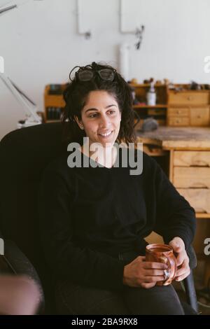 Taille-up-Porträt von sitzenden weiblichen Juwelierin in Kalifornien Home Studio Stockfoto