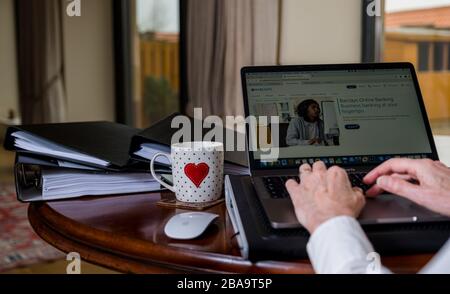 Frau, die zu Hause auf einem Laptop auf dem Tisch arbeitet und auf dem Bildschirm die Online-Banking-Website von Barclays angezeigt wird Stockfoto