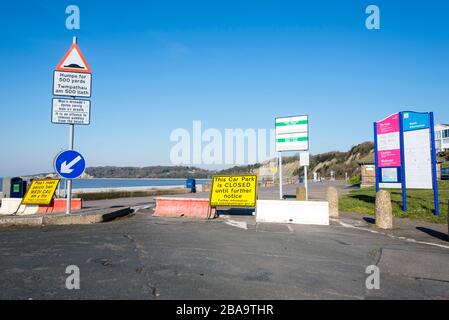 An einem sonnigen Tag ist der Zugang zu einem Parkplatz am Meer während der Krisen des Coronavirus durch eine temporäre Barriere blockiert. Schilder auf Walisisch und Englisch Stockfoto