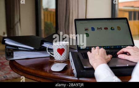 Frau, die zu Hause auf einem Laptop auf dem Tisch arbeitet und Google-Anwendungen auf dem Bildschirm anzeigt Stockfoto
