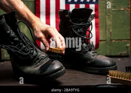 Mann poliert alte Militärstiefel vor der Flagge der USA Stockfoto