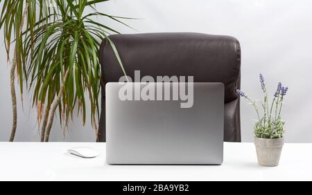 Ein offener grauer Laptop steht auf einem weißen Tisch neben einer kabellosen Maus, dem Arbeitsplatz eines freiberuflichen Unternehmers, nahe der weißen Wand Stockfoto