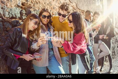 Fröhliche junge Freunde, die Spaß haben, Smartphones zu sehen. Fröhliche Studenten genießen einen sonnigen Tag, an dem sie mit ihren Handys spielen und Social Med nutzen Stockfoto