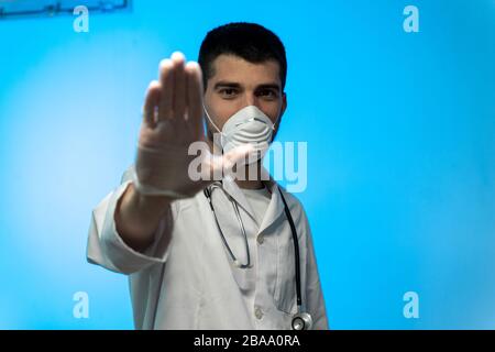 COVID 19 Concept stoppen. Junger Arzt in medizinischer Uniform mit einer schützenden Gesichtsmaske und Handschuhen, die Stop Hands Geste für Stop Coronavirus Ausbruch zeigen Stockfoto