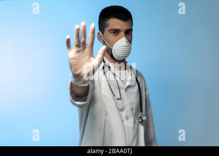 COVID 19 Concept stoppen. Junger Arzt in medizinischer Uniform mit einer schützenden Gesichtsmaske und Handschuhen, die Stop Hands Geste für Stop Coronavirus Ausbruch zeigen Stockfoto