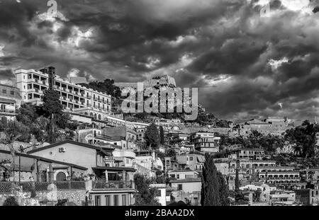 Schöner Blick auf das bewohnte Zentrum der Bergstadt Taorminas, Messina, Sizilien, Italien, gegen einen dramatischen Himmel, schwarz-weiß Stockfoto