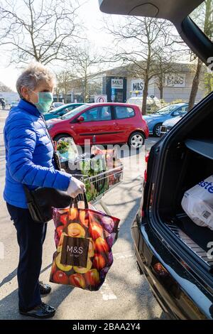 Southampton, England, Großbritannien. 2020. Eine ältere Frau, die während der Coronavirus-Epidemie eine Gesichtsmaske und Gummihandschuhe trägt und Einkaufen in ein Auto lädt Stockfoto