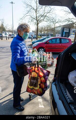 Southampton, England, Großbritannien. 2020. Eine ältere Frau, die während der Coronavirus-Epidemie eine Gesichtsmaske und Gummihandschuhe trägt und Einkaufen in ein Auto lädt Stockfoto