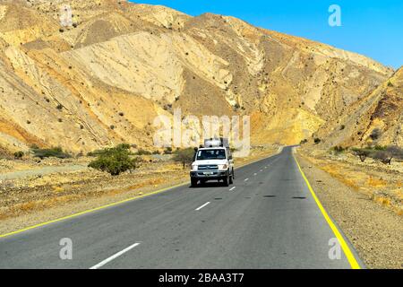 Geländewagen mit Touristen, die auf einer modernen Asphaltstraße in einem ariden Tal in der Nähe von Berhale, Afar-Region, Äthiopien fahren Stockfoto