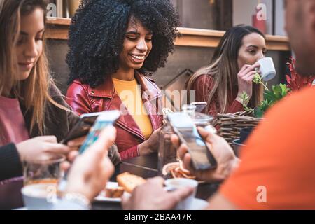 Gruppe junger Leute, die in einem Café sitzen und die Anwendung der sozialen Medien auf dem Smartphone nutzen. Junge Männer und Frauen treffen sich mit dem Handy am Café-Tisch Stockfoto