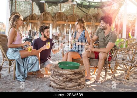 Fröhliche Freundschaftsgruppe, die Spaß an Strandparty hat, Cocktail bei Sonnenuntergang zu trinken - Sommerfreude und Freundschaftskonzept mit jungen Menschen im Urlaub - warme Sonne Stockfoto