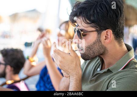 Eine Gruppe von Freunden, die am Strandkiosk Cocktails genießen. Junge Freunde, die Spaß haben, draußen zu jubeln, konzentrieren sich auf die Hand. Glück und Zusammenleben Stockfoto