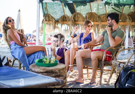 Eine Gruppe von Freunden, die am Strand Cocktails trinken und Zigaretten rauchen. Stockfoto