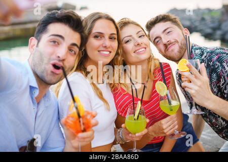 Gruppe der besten Freunde, die Spaß haben, Selfies mit Smartphone zu machen und bunte Cocktails am Meer zu trinken Stockfoto