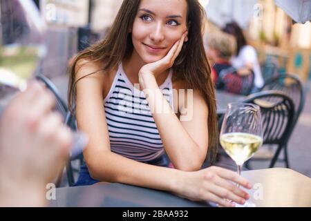 Ein romantisches Paar trinkt Weißwein im Freien im Tischrestaurant. Konzentrieren Sie sich auf die Augen junger Mädchen, die die Augen ihres Freundes verwässern. Außenaufnahmen Stockfoto