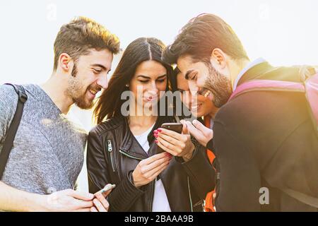 Junge Freunde, die im Freien einen Rucksack tragen und ein Smartphone sehen. Junge Frau, die etwas Interessantes für Freunde zeigt. Sommerhinterleuchtung. Stockfoto