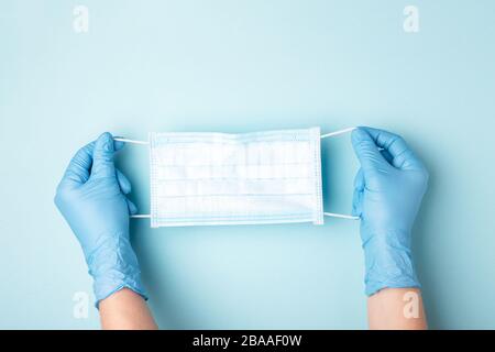 Hände in Handschuhen mit medizinischer Gesichtsmaske auf blauem Hintergrund. Vorbeugende Maßnahmen zum Schutz vor Virusinfektionen. Stockfoto