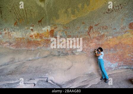 Ein Tourist fotografiert die Kunst des San Rock in der Inanke Cave, Matobo National Park, Simbabwe. Stockfoto